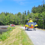 Rettungshubschrauber Christoph20 im Notfalleinsatz, auf dem Damm am Fichelsee gelandet. Im Hintergrund weitere Einsatzfahrzeuge der Rettungskräfte.