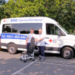 Schulungstag des BRK-Patientenfahrdienst Bayreuth - Mitarbeitende des BRK-Patientenfahrdienstes und ein Tragestuhl vor Spezial-Fahrzeug.