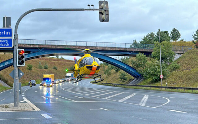 Das Bild zeigt einen auf der Bundestraße landenden Rettungshubschrauber der ADAC-Luftrettung. Im Hintergrund sind weitere Einsatzfahrzeuge und stauender Verkehr zu sehen.