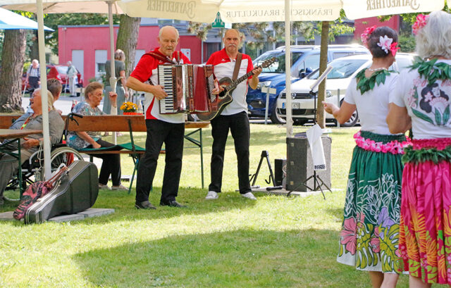 Bild zeigt das musikalische Duo "Frankentop" beim Sommerfest des BRK-Ruehsitzes. Im Vordergrund Tänzerinnen der Tangrzuppe "Lau Hala".