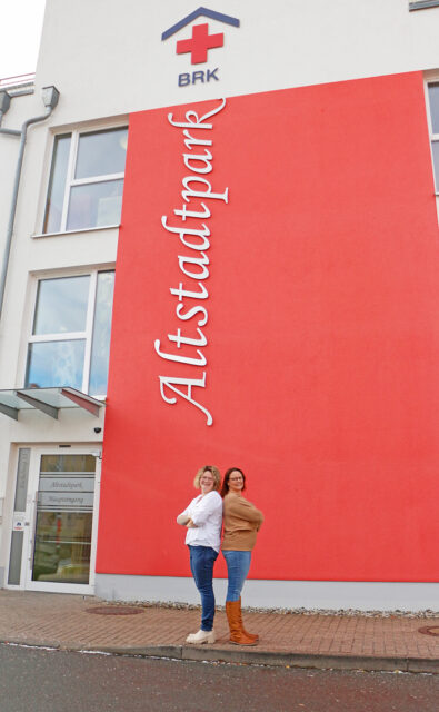 Katja Gutmann (r.) und Daniela Geißler (l.) vor dem Eingang des BRK-Altstadtparks. Im Hitnergrund der Schriftzu Altstadtpark an der Wand.