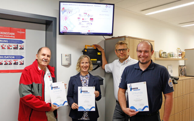 Zu sehen: Karl Bernet (l.) mit Chrsitine Bernet, Markus Ruckdeschel (BRK-Kreisgeschäftsführer Bayreuth) und Dr. Christopher Häfner (Leiter der ILS Bayreuth/Kulmbach) mit den Auszeichnungs-Ukunden des Bayerischen Staatsministeriums des Innern für den Bayerischen Engagiert Preis 2024.