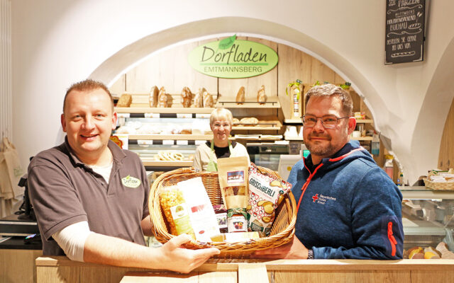 Zu sehen ist: Der Dorfladen Emtmannsberg mit einer Theke mit Backwaren. Hitner der Theke steht eine ehrenamtliche Mitarbeiterin. Stefan Bauernfeind (l.) und Florain Förster (r.) halten einen Korb mit regionale Waren, die im Emtmannsberger Dorfladen angeboten werden.