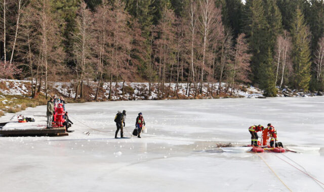 Zusehen sind Taucher auf dem gefrorenen Fichtelsee, sowei sicherende Mitglieder der Wasserwacht.